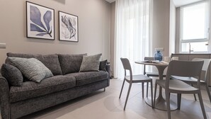 A modern living room with a grey sofa, a dining table with chairs, and two framed artworks on the wall. - Italianway Comfort - Maderno 4 (Milano)