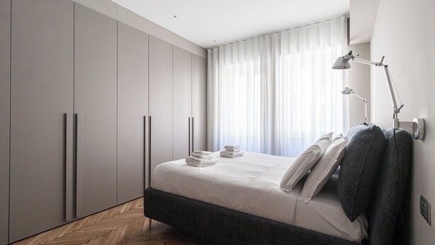 A modern bedroom with a bed, grey wardrobe, and a desk lamp. - Italianway Comfort - Maderno 4 (Milano)