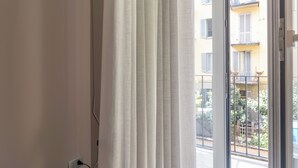 A room with a window, a curtain, and a visible balcony with plants and a fence. - Italianway Comfort - Maderno 4 (Milano)