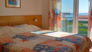 A bedroom with a bed, a headboard, a nightstand, a window with curtains, and a painting on the wall. - Apartments Lavanda & More (Rab)