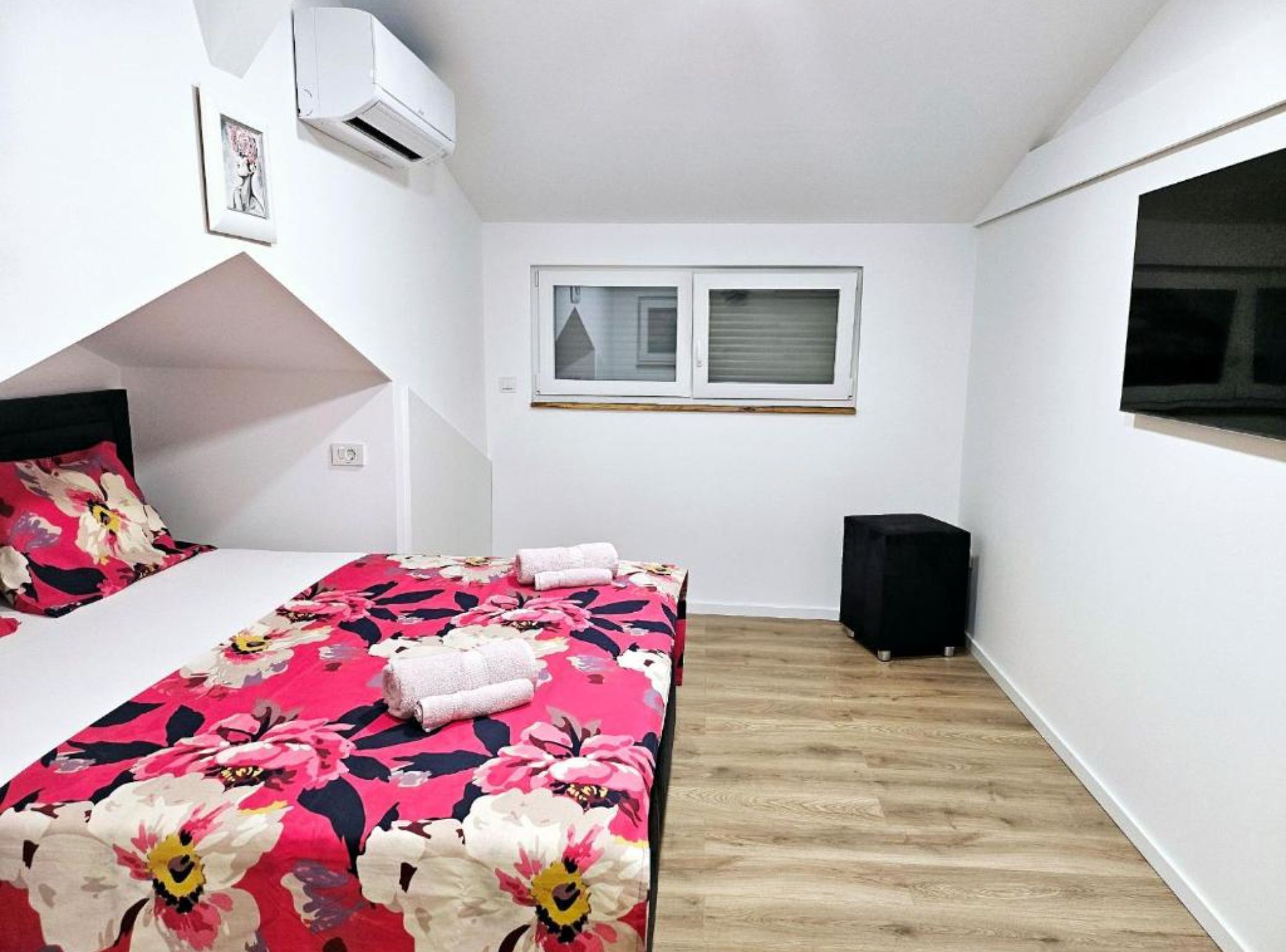 A bedroom with a bed, a window, an air conditioning unit, and a black speaker.