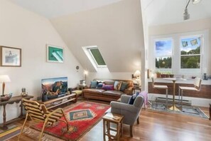 A spacious loft apartment with a high ceiling, a large window offering a view of the outdoors, a cozy seating area with a sofa and armchairs, and a dining area with a table and chairs. - The Miners Union: Hip & Historic (Telluride)