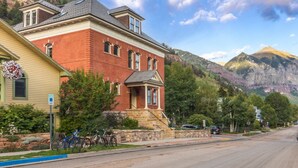 A two-story red brick building with a stone foundation, a front porch, and a clear view of a mountain range in the background. - The Miners Union: Hip & Historic (Telluride)