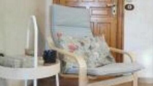 Una habitación con una puerta de madera, una silla blanca y una pequeña mesa.
