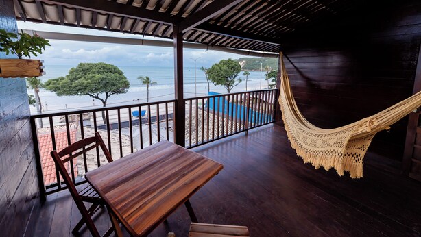 A wooden deck with a hammock, a table, and chairs overlooking a beach. - Pousada Terra do Sol Natal (Natal)