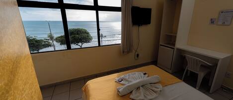 A hotel room with a bed, a desk, a TV, and a window with a view of the ocean.