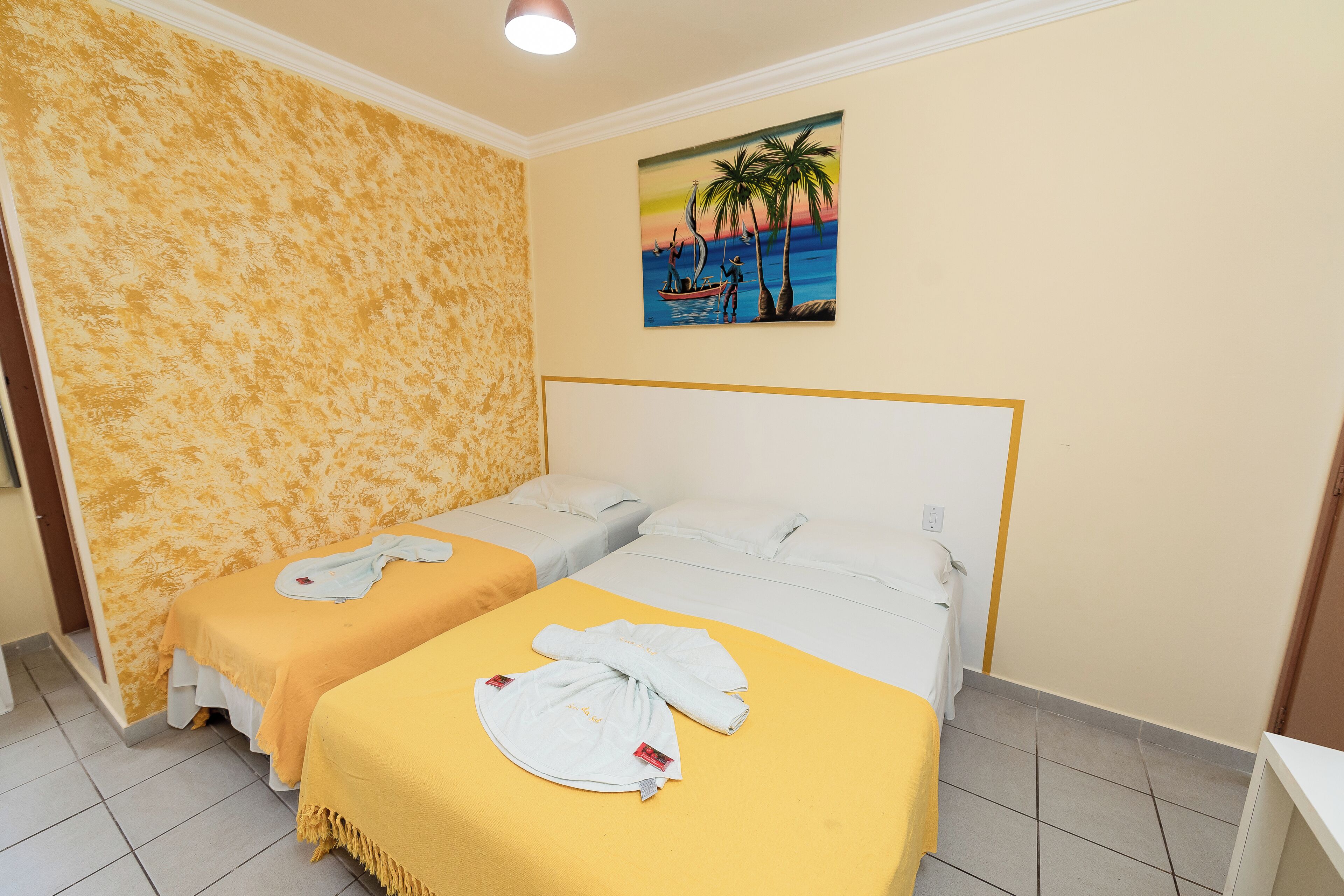 A hotel room with two beds, a painting of a beach scene, and a yellow bedspread.