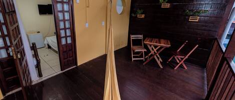 Una stanza con pavimento in legno, un'amaca, una sedia di legno, un tavolino e una TV fissata al muro.
