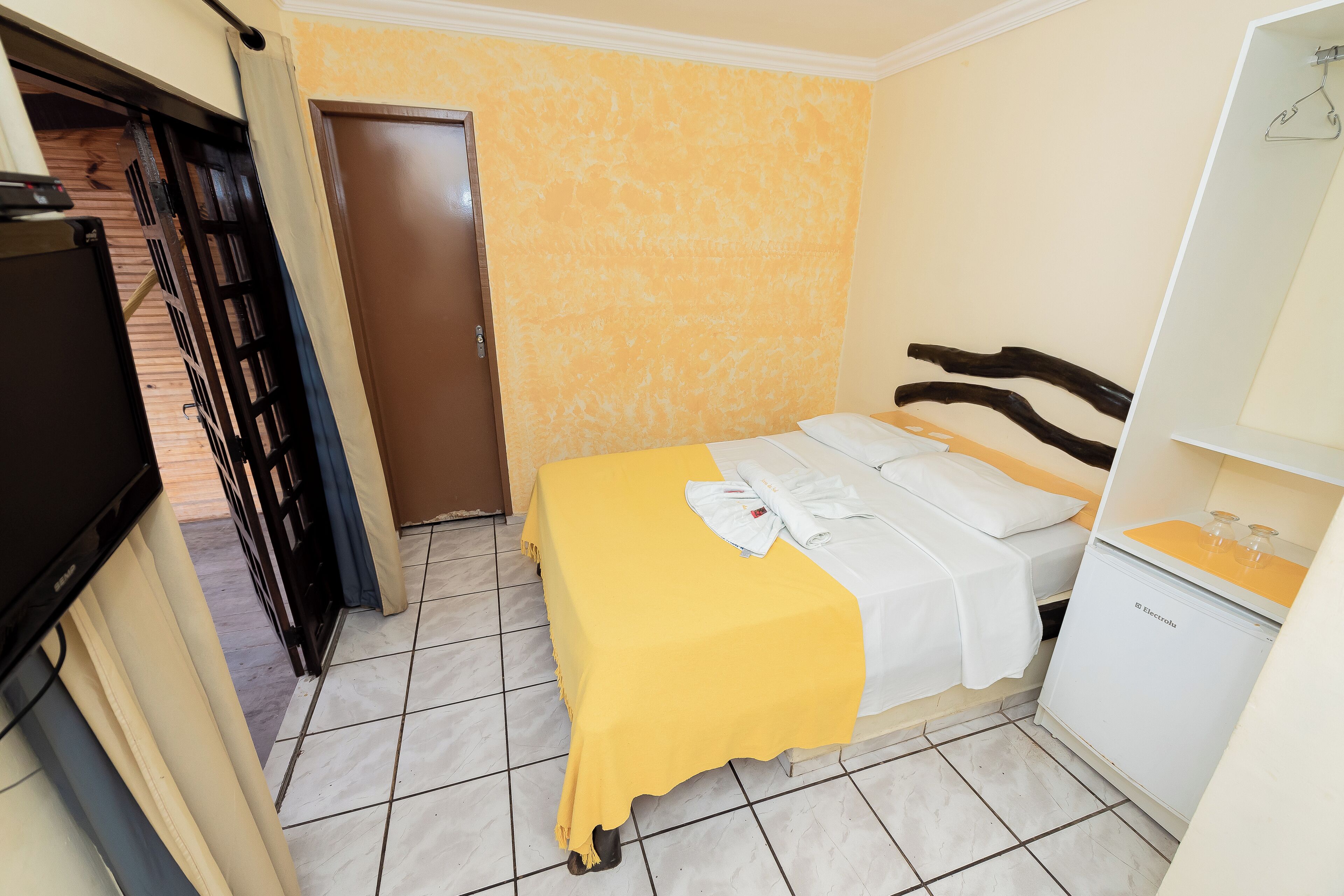A small hotel room with a bed, a wardrobe, and a television.
