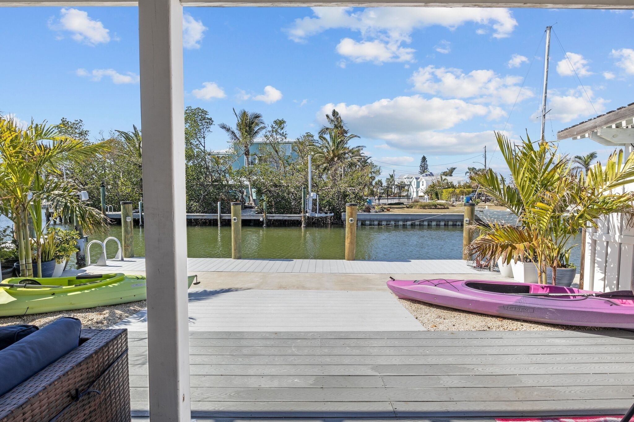 A wooden dock with kayaks and a view of a marina with boats and palm trees.