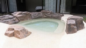 Un bain à remous entouré de gros rochers et bordé d’une zone sablonneuse.
