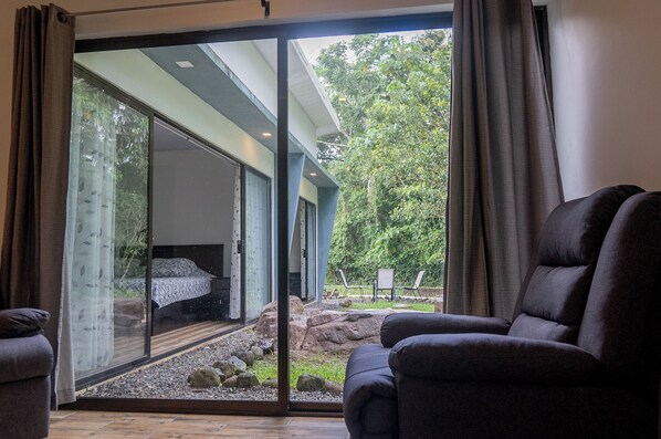 Un intérieur moderne avec une grande porte-fenêtre coulissante donnant sur une chambre à coucher, équipée d’un lit et offrant une vue sur un jardin.