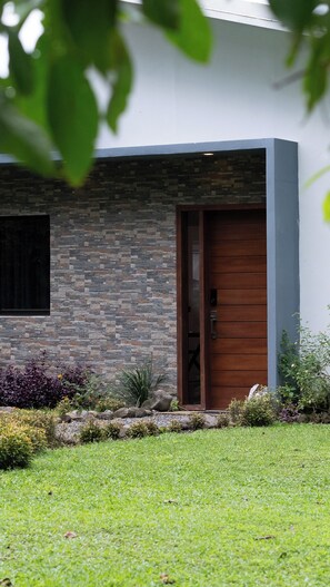 Une maison moderne avec une façade en pierre, une porte en bois et un petit jardin agrémenté de diverses plantes.