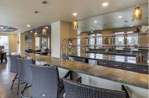 A modern kitchen with a long counter, bar stools, and pendant lighting.
