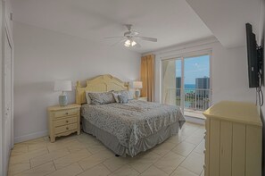 A bedroom with a bed, nightstands, a ceiling fan, a TV, and a view of the ocean through a sliding door. - Ariel Dunes II 907 *Beach views *Pools* (Miramar Beach)