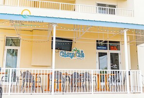 A building with a sign for 'Cabana Cafe' and 'Bud Light' on the window. There is a balcony with a white railing and string lights. - Ariel Dunes II 907 *Beach views *Pools* (Miramar Beach)