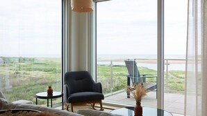 Een moderne woonkamer met een groot raam met uitzicht op een strand en een grasland.