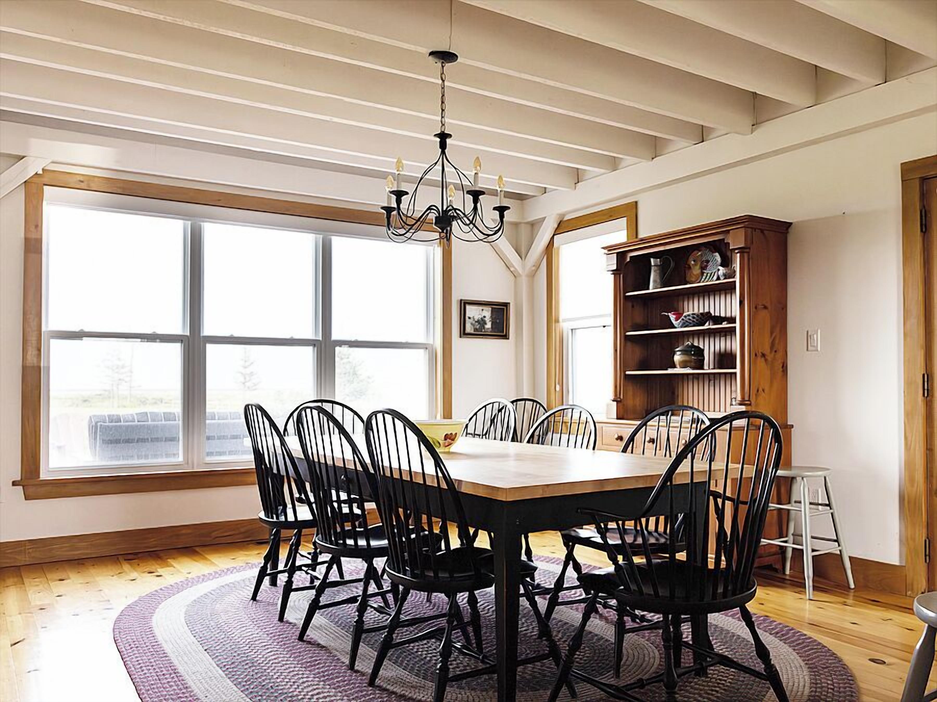 A dining room with a large window, a chandelier, and a wooden bookshelf.