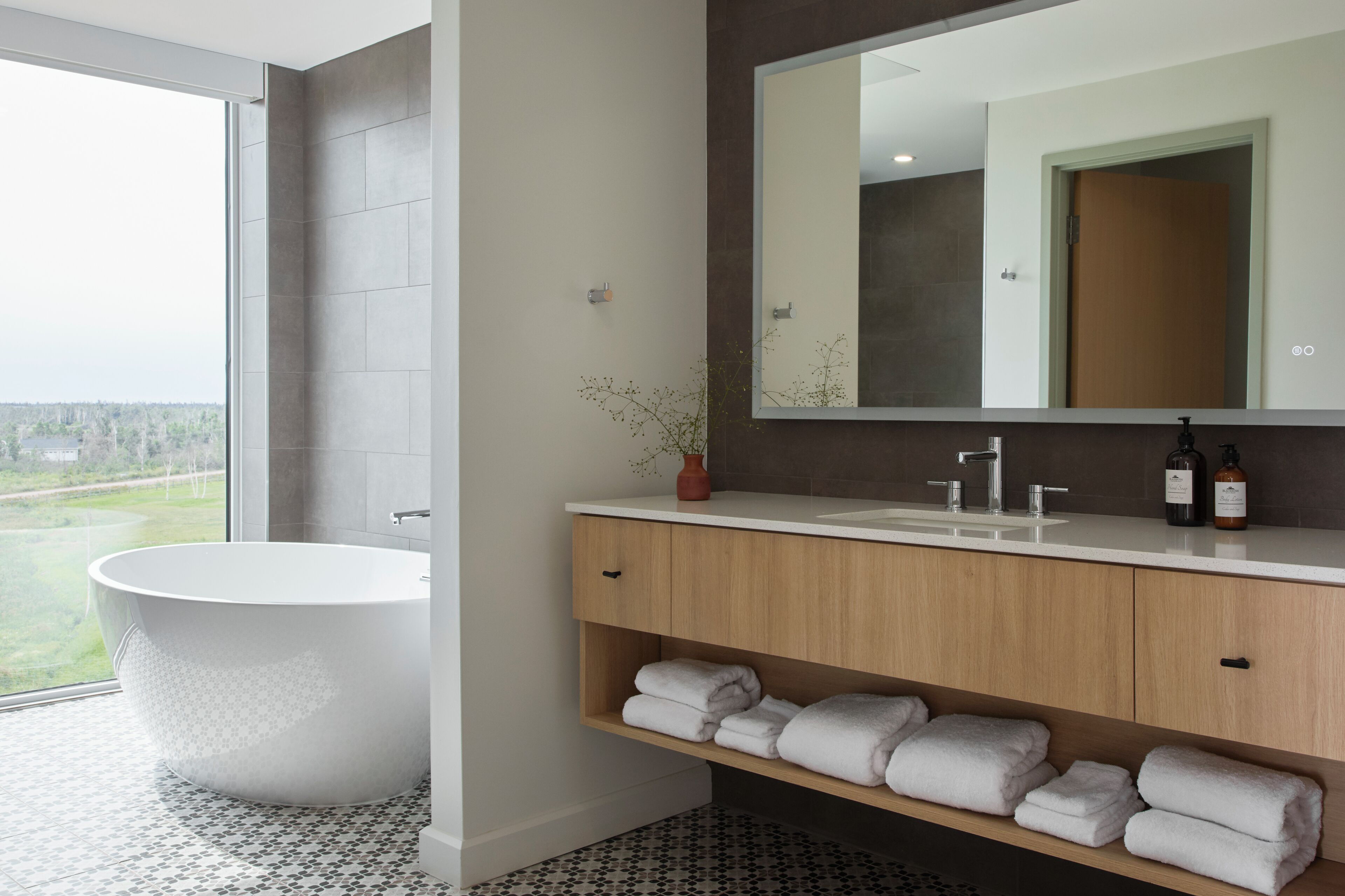 A modern bathroom with a freestanding bathtub, a large mirror, and a vanity with shelves for towels.