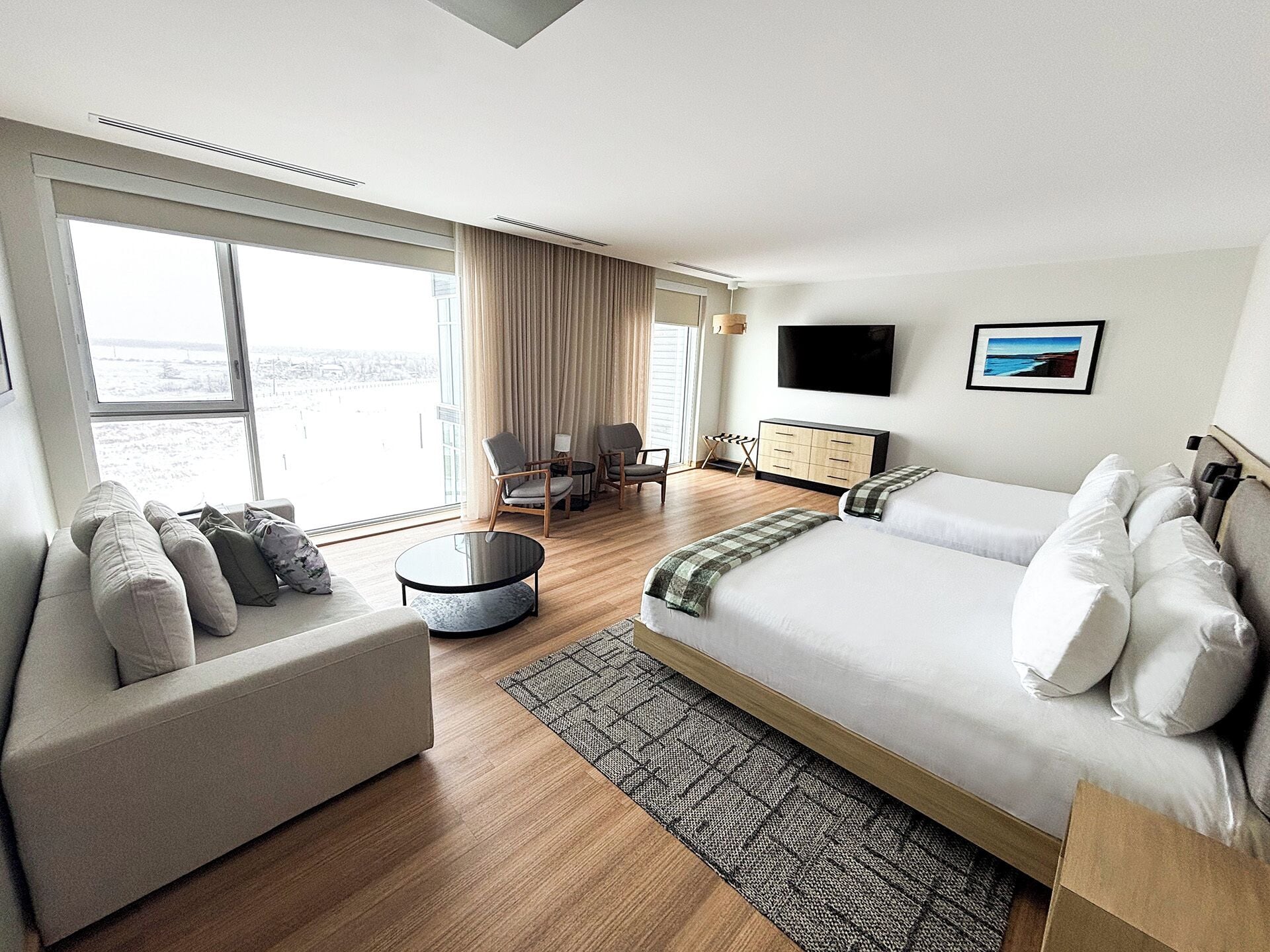 A modern hotel room with a large bed, a sofa, a round coffee table, and a TV.