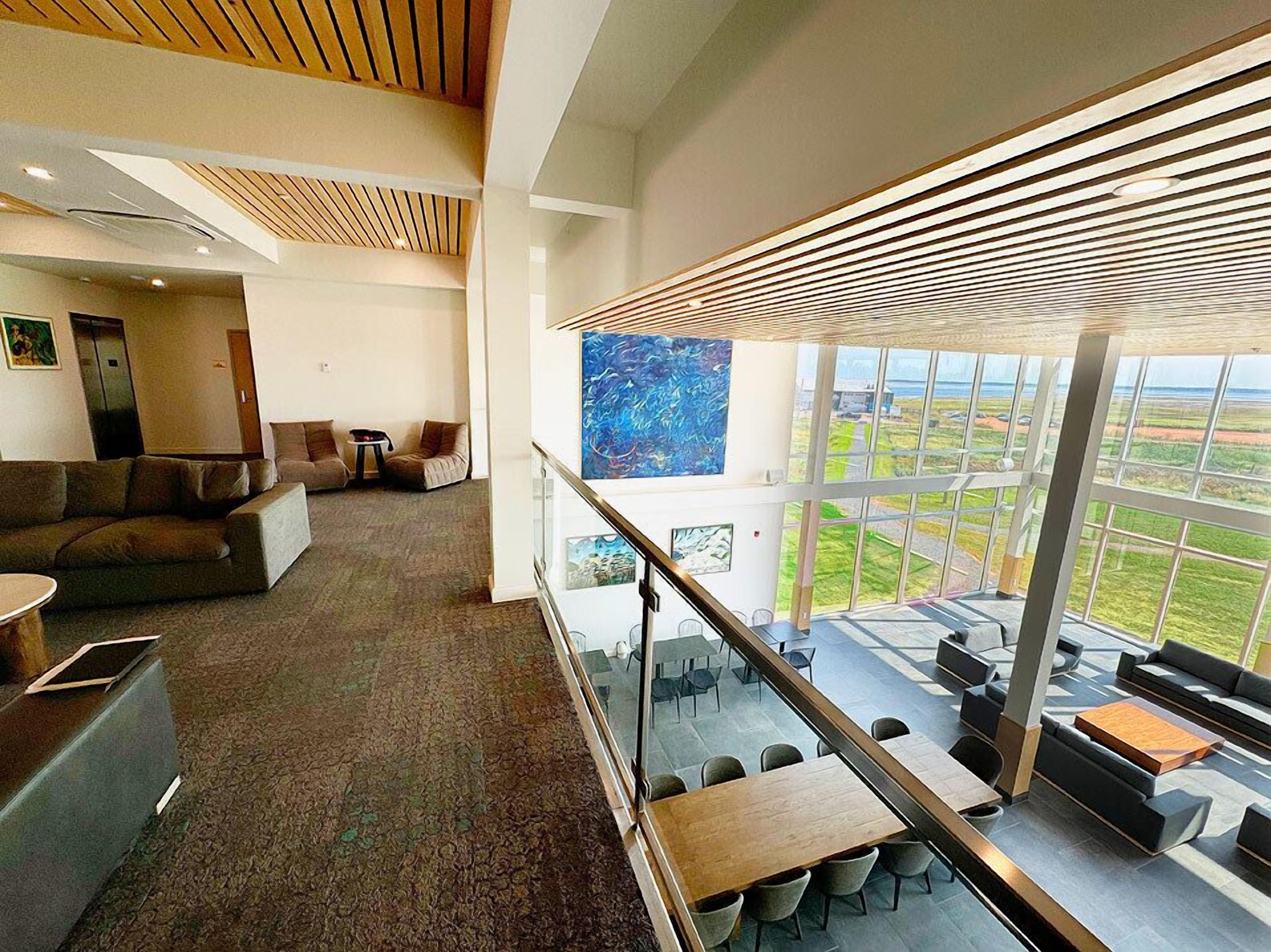 A spacious lobby with a high ceiling, a seating area with couches and chairs, a reception desk, and a large window offering a view of the outdoors.