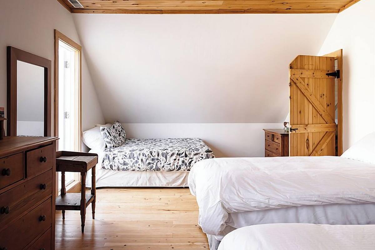 Ein Schlafzimmer mit schrägem Dach, Holzboden, einem Bett mit weißer Bettwäsche, einem Schminktisch und einem Kleiderschrank.