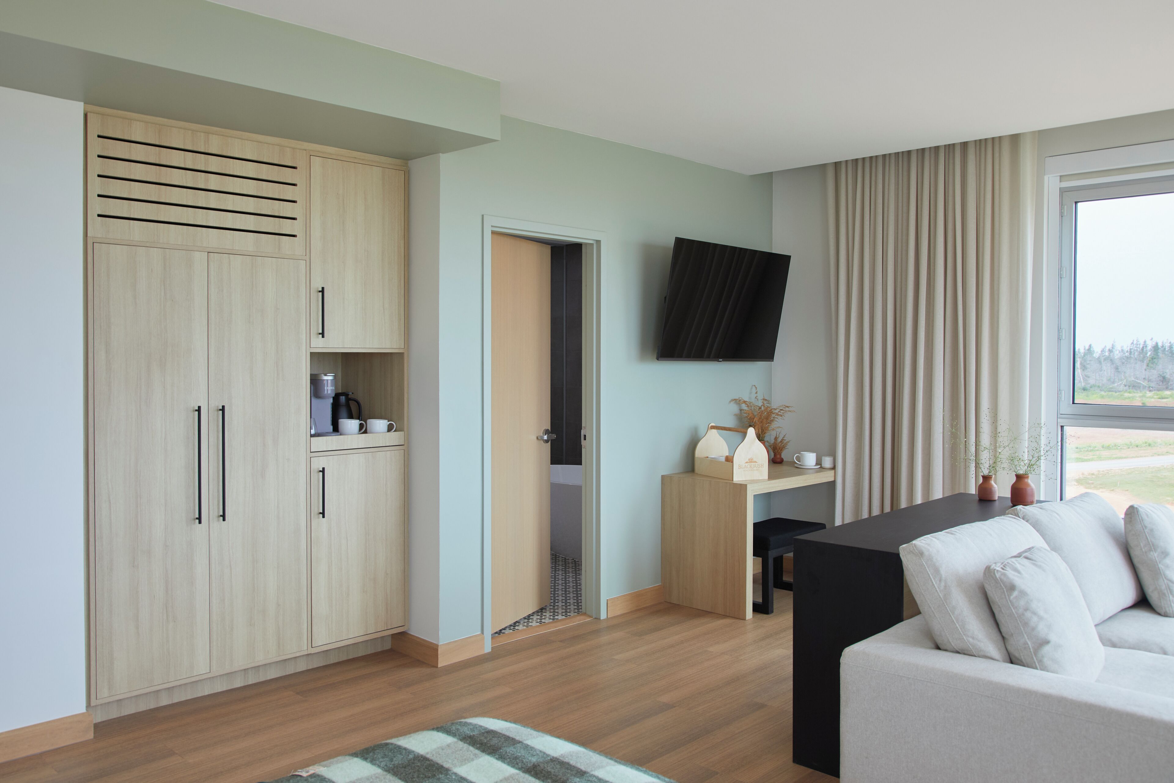 Una habitación moderna con kitchenette, TV de pantalla plana, sofá y un amplio ventanal con cortinas.
