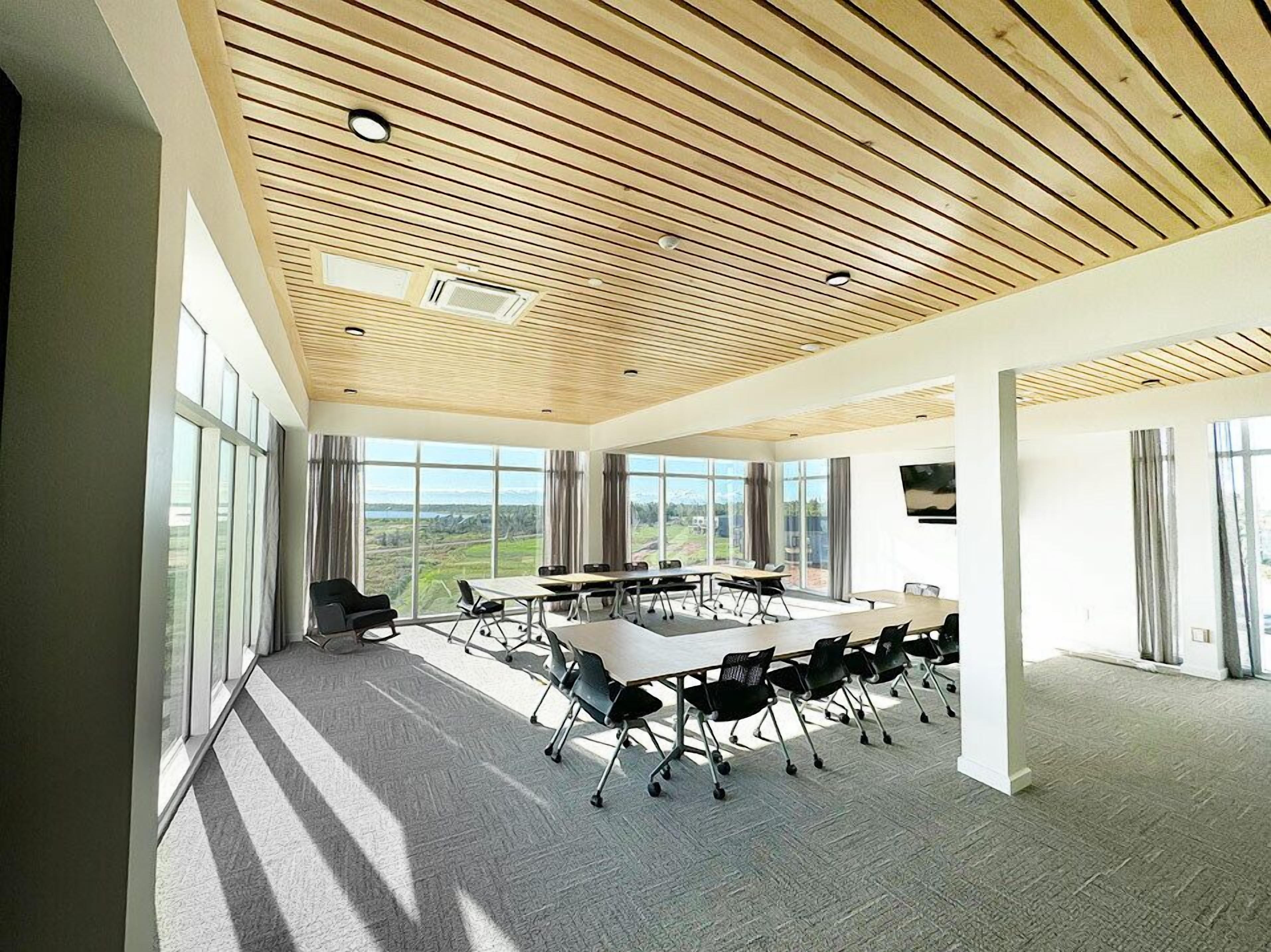 A modern conference room with a large table, chairs, and large windows offering a view of the outdoors.