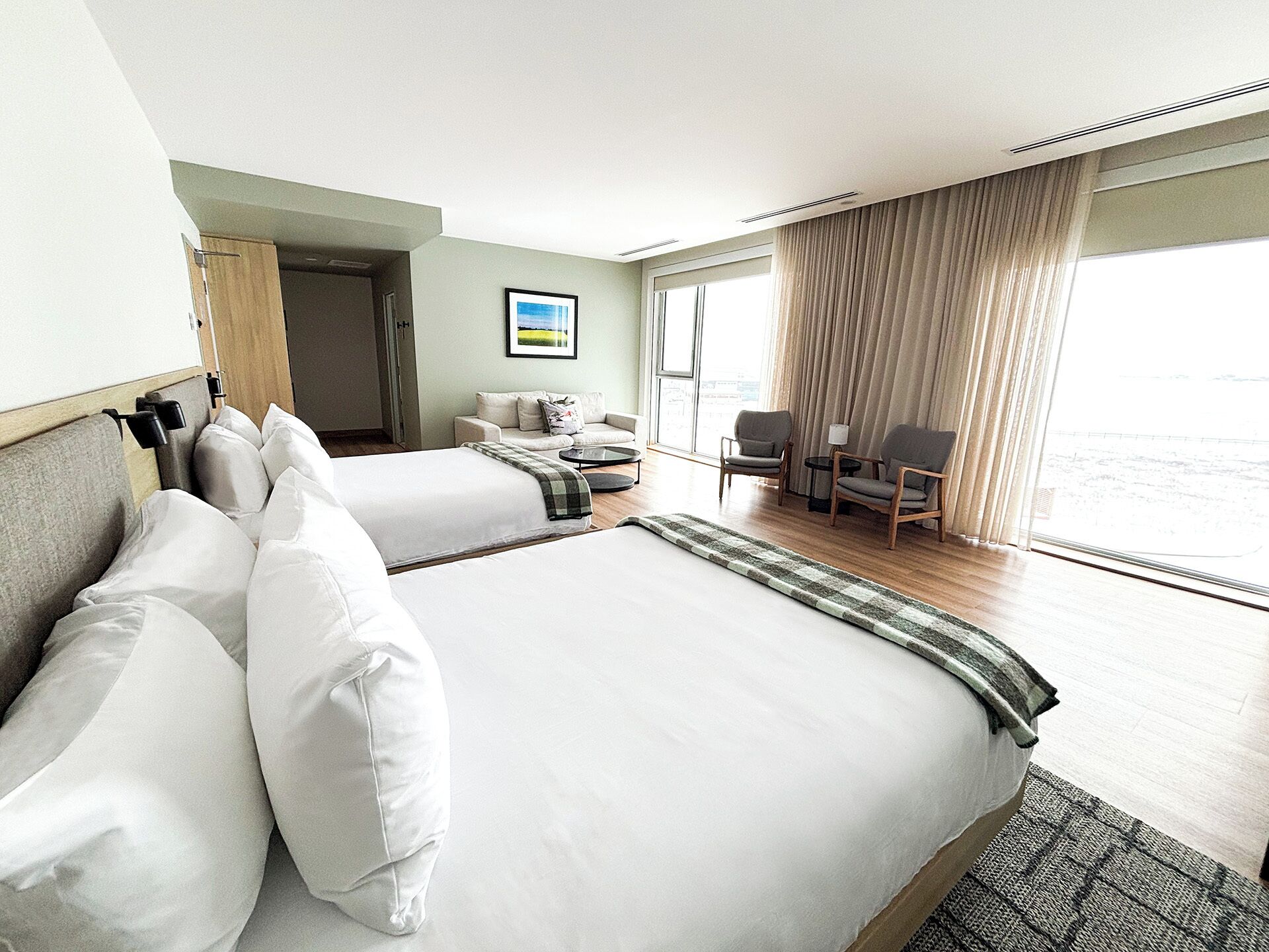 A hotel room with two beds, a sofa, a small table, and a view of the sea.