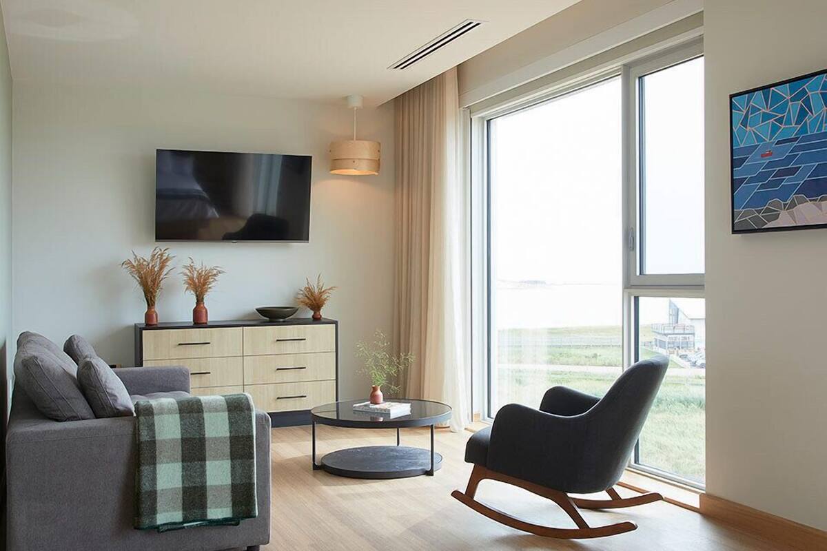 Ein modernes Wohnzimmer mit einem grauen Sofa, einem schwarzen Schaukelstuhl, einem runden Couchtisch und einem Fernseher an der Wand.