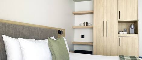 A hotel room with a bed, a wardrobe, and a shelf with items.