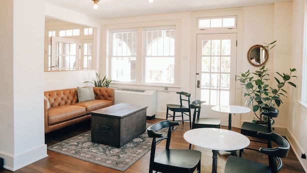 A bright living room with a brown leather sofa, a coffee table, and a dining area with chairs and a table. - Westphalia Inn (Westphalia)