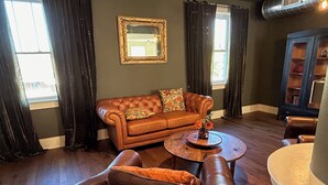 A living room with a brown leather sofa, a round coffee table, and a dark-colored armchair. - Westphalia Inn (Westphalia)