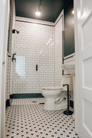 A bathroom with white subway tiles, a white toilet, and a black floor lamp. - Westphalia Inn (Westphalia)