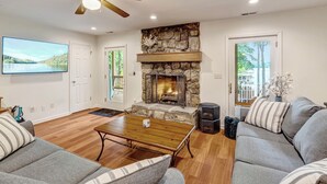 A living room with a stone fireplace, a ceiling fan, and a large TV on the wall. - Luxurious Water Front Home, Main Lake View (Bracey)