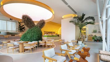 Et moderne interiør med et centralt siddeområde, en bar og en stor planteskulptur.