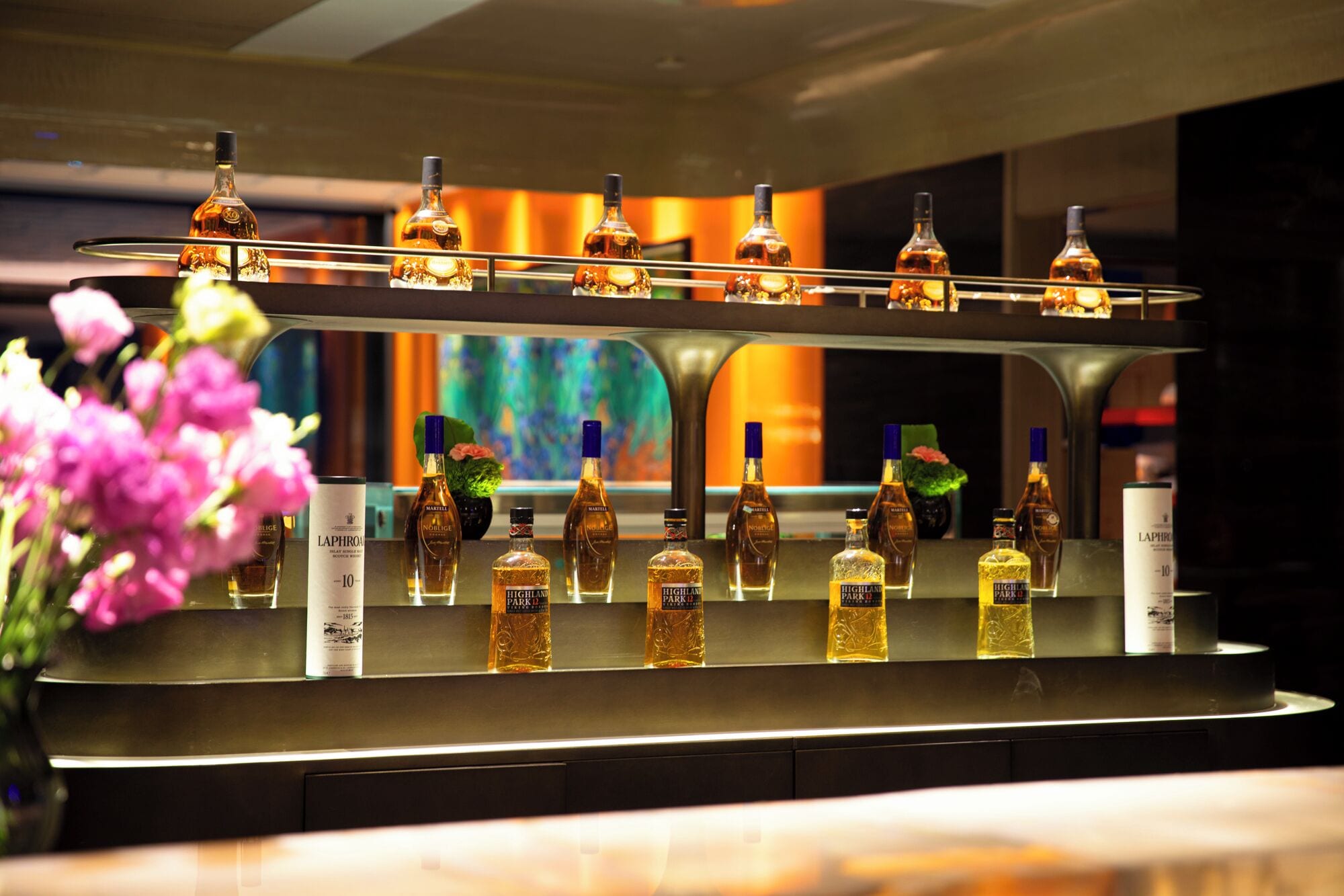 A bar area with multiple bottles of whisky and a decorative vase of flowers.