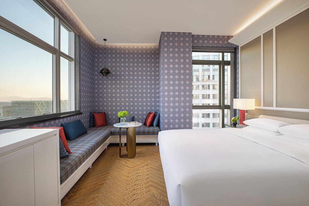 Ein Hotelzimmer mit einem großen Bett, einer Sitzecke mit Blick und einem kleinen Tisch mit Lampe.