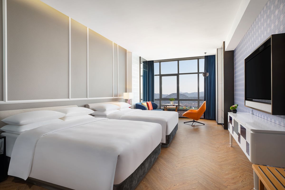 Ein Hotelzimmer mit zwei Betten, einem Fernseher, einem großen Fenster mit Aussicht und Holzboden.