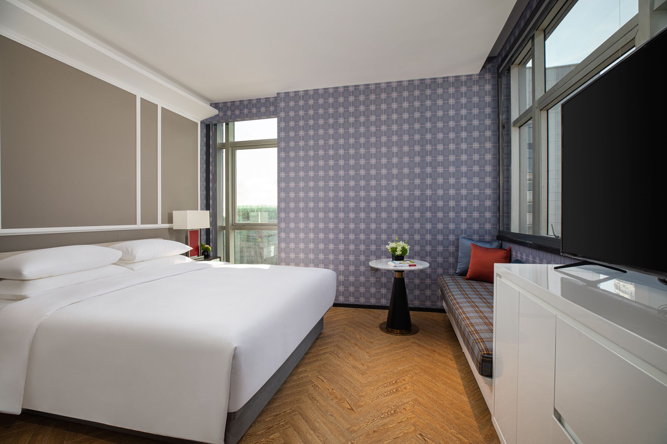 Habitación de hotel con una cama grande, una mesita con una planta, un sofá y un televisor.