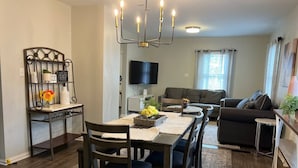Comedor con una mesa, sillas, una araña, televisor, sofá y ventana con cortinas.