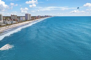 Eine Küstenstadt mit einem langen Strand, Hochhäusern und blauem Himmel.