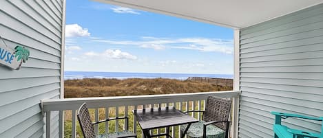 Un balcon donnant sur la plage, une table, deux chaises et un panneau sur le mur.