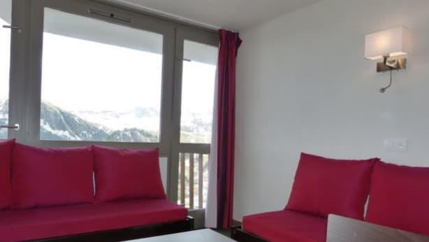 Ein Zimmer mit einem weißen Tisch, zwei roten Sofas, einem Fenster mit Bergblick und einer Wandleuchte.
