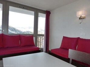 Ein Zimmer mit einem weißen Tisch, zwei roten Sofas, einem Fenster mit Bergblick und einer Wandleuchte.