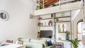 En rummelig opholdsstue med hvælvet loft, spisebord, sofa og fjernsyn.