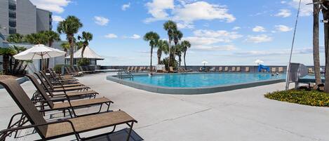 A poolside area with lounge chairs, umbrellas, and palm trees.