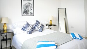 A neatly arranged hotel room with a bed, two bedside tables, a large mirror, and a framed picture on the wall. - Fun Energetic Oasis in Islington - Sleeps6 (London)