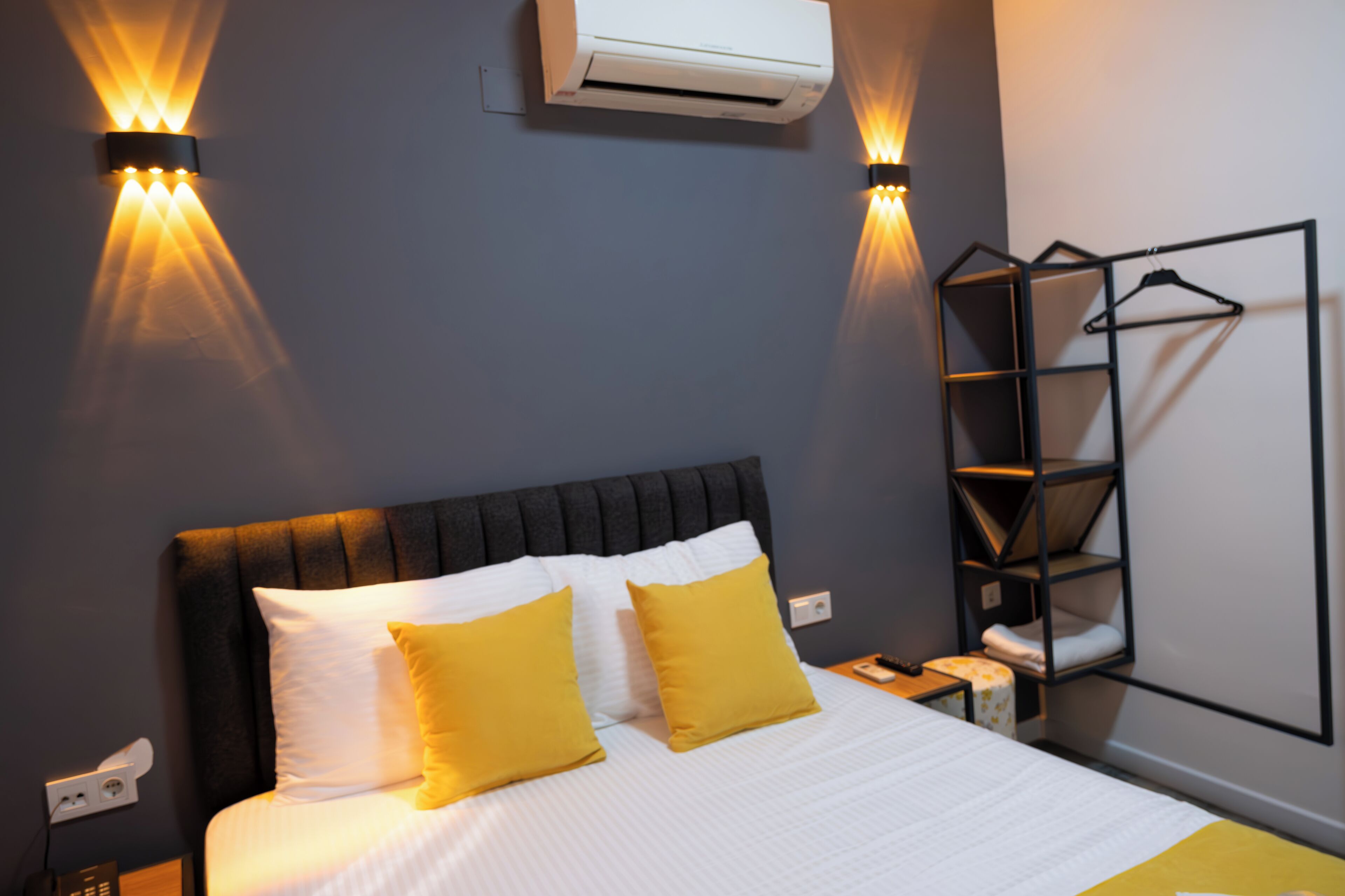 A neatly made bed with white and yellow bedding, a black headboard, and two wall-mounted lights.