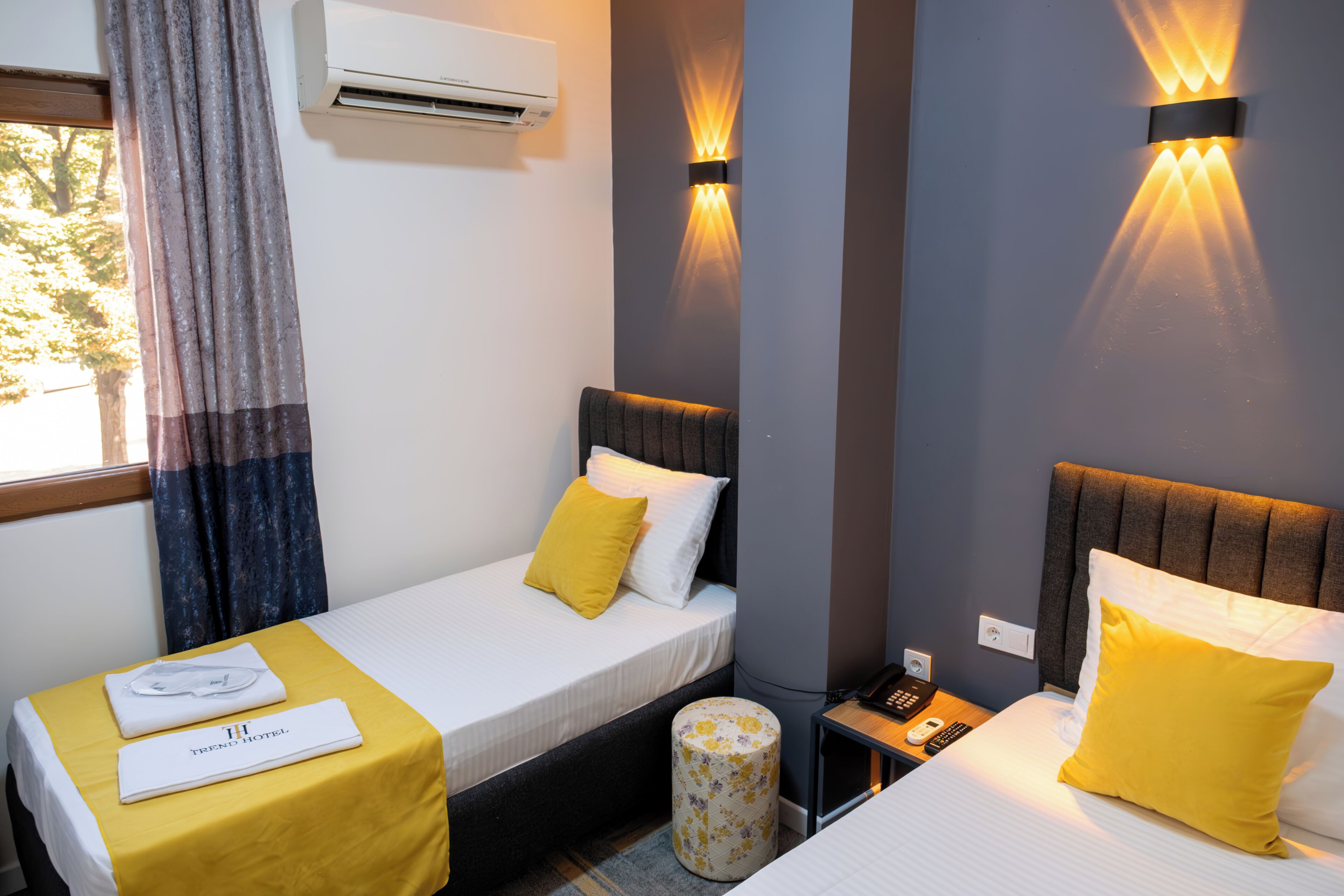 Hotelkamer met twee bedden, een tafeltje, een airconditioner en een nachtkastje met een telefoon.